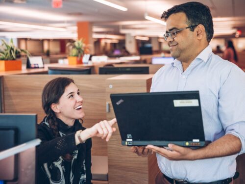 Coworkers, a seated woman and a standing man, in cheerful discussion