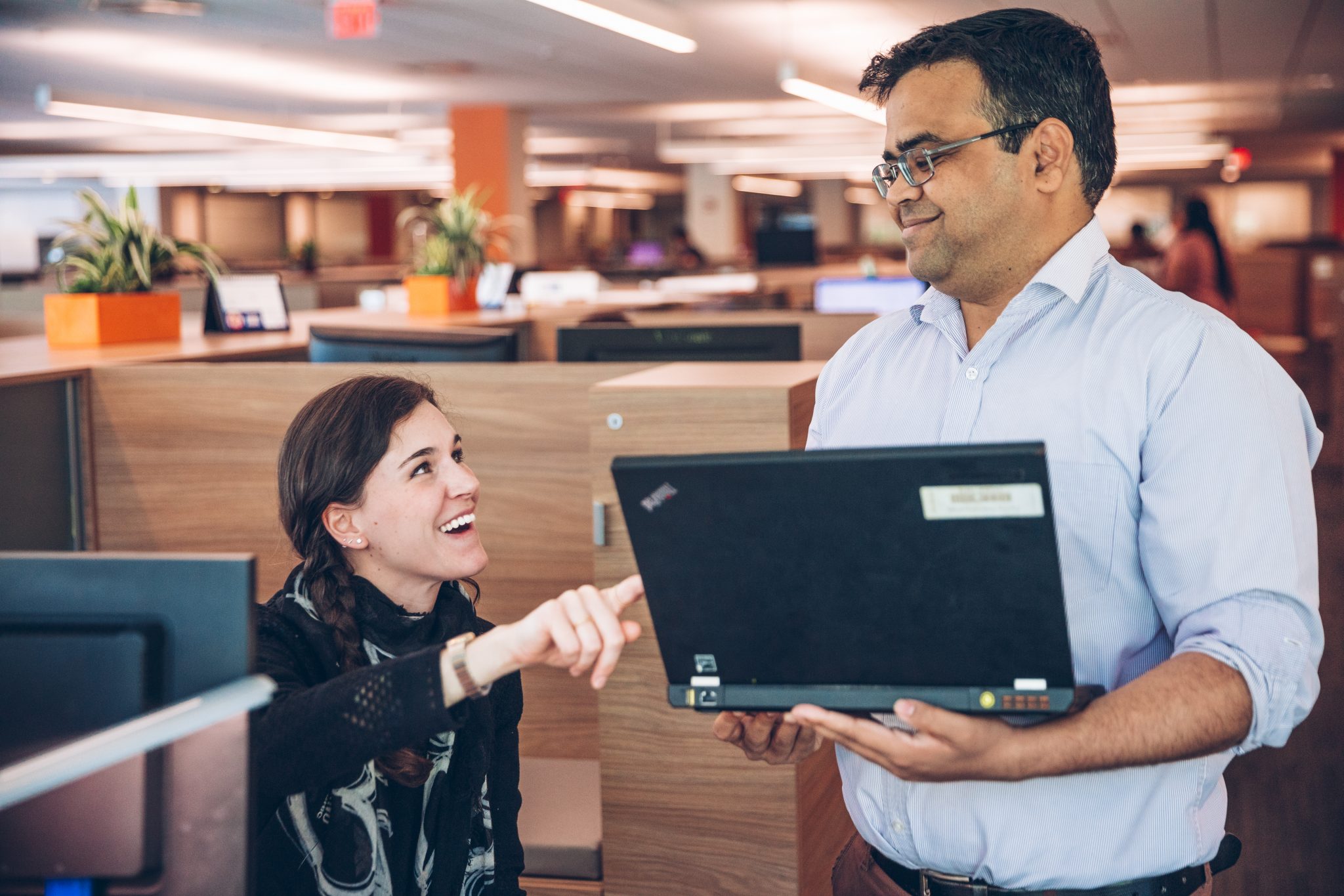 Coworkers, a seated woman and a standing man, in cheerful discussion