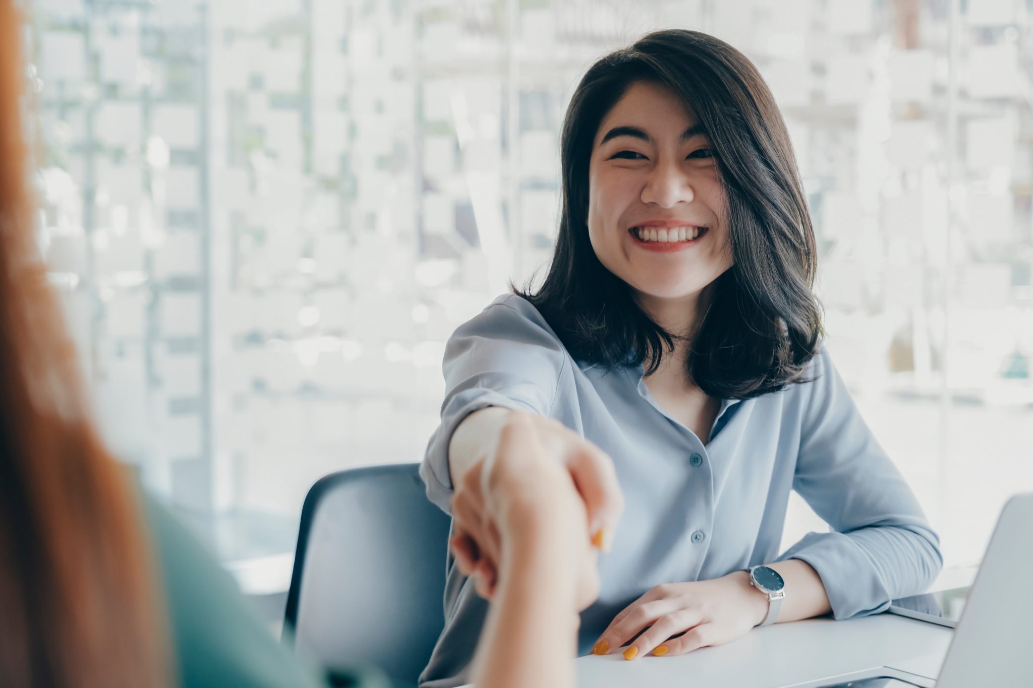 Young women shaking hands seated at a desk